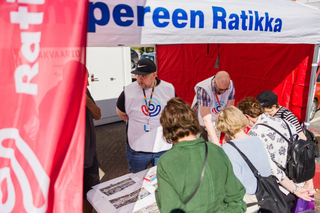 Henkilöitä suunnittelukarttojen ympärillä Tampereen Ratikan pisteellä yleisötilaisuudessa.